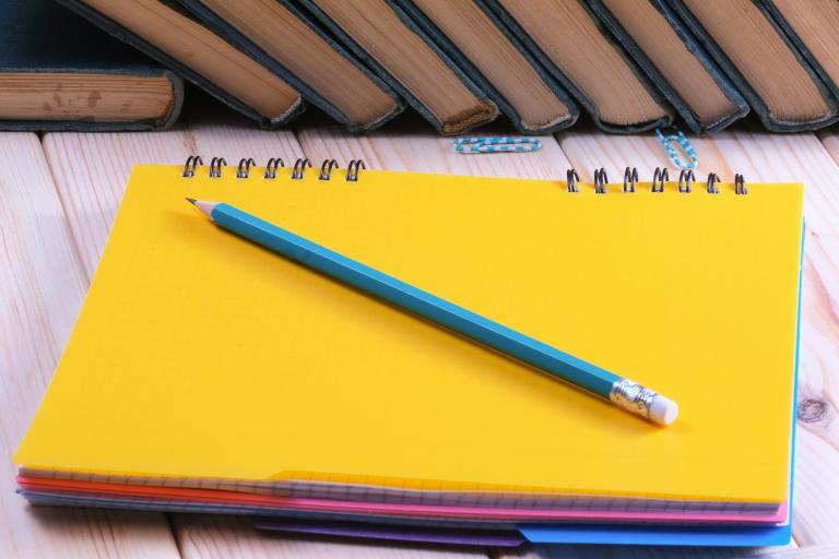 notepad and pencil, with a row of books in the background